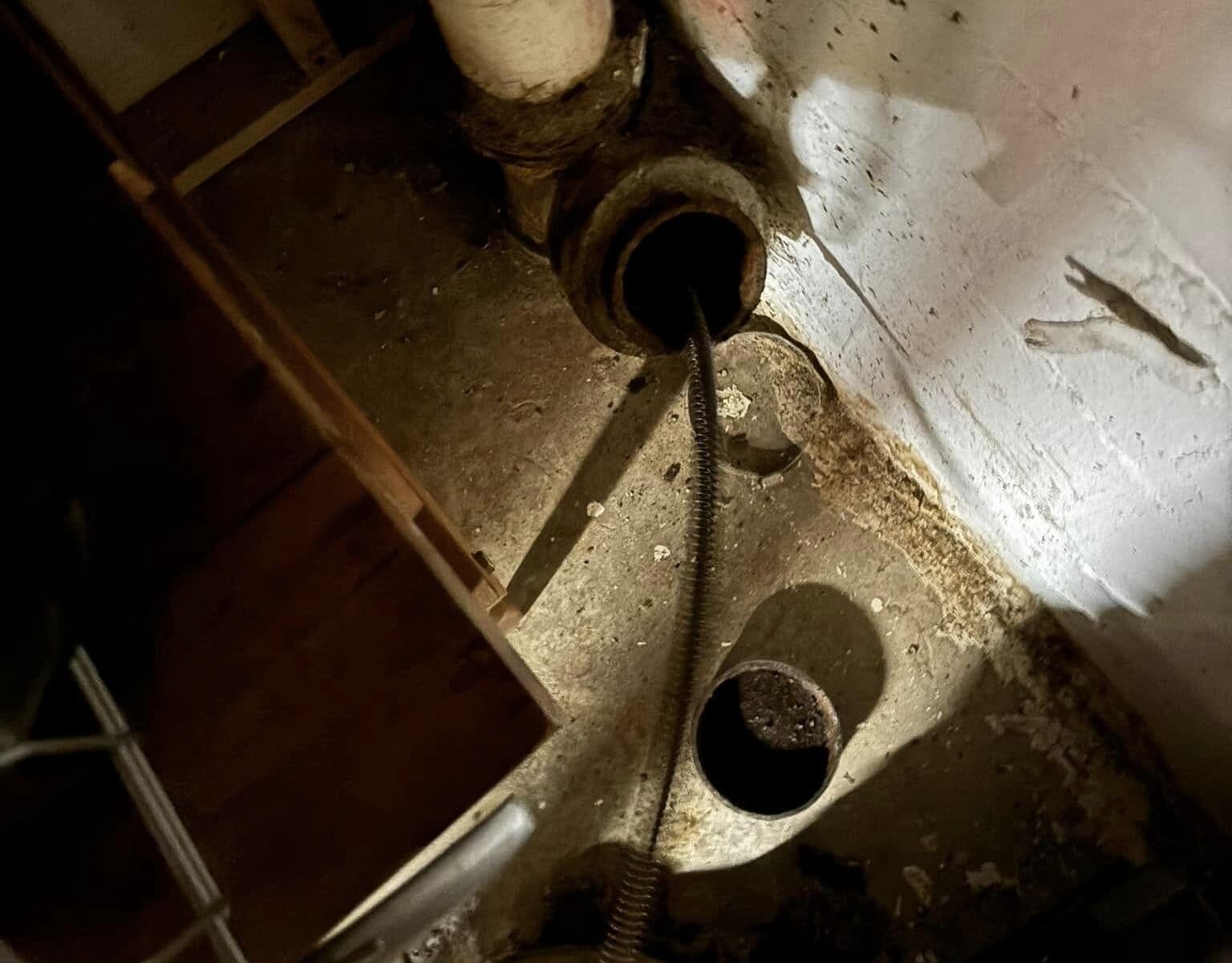 Drain Bros llc fixes a sewer line issue in a basement, using tools to clear clogs and repair pipes under the floor.