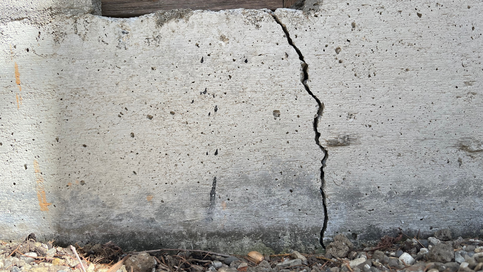 Concrete wall crack at base shows potential drainage or sewer issues—Drain Bros llc can help fix these problems.
