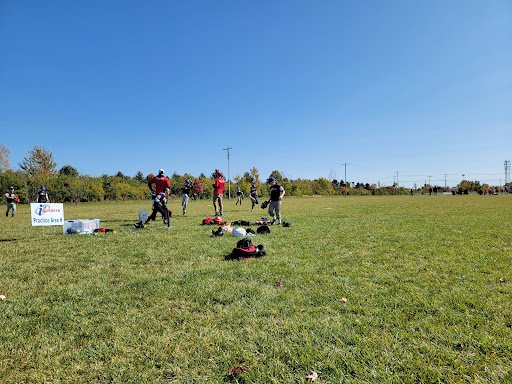 Kids are practicing sports on a field with Drain Bros LLC prepping an area for new drainage to help the field stay dry.