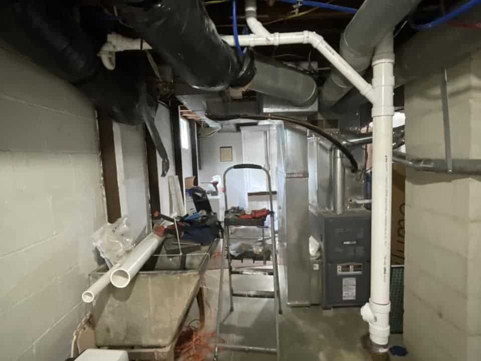 Drain Bros llc can help with sewer line issues shown by exposed pipes and tools in this unfinished basement.