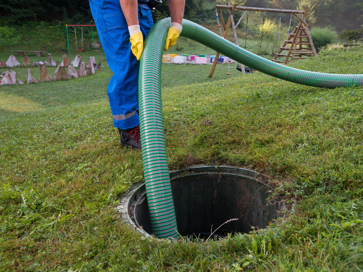 Drain Bros llc worker services a septic tank outdoors, showing professional care in residential septic system maintenance.