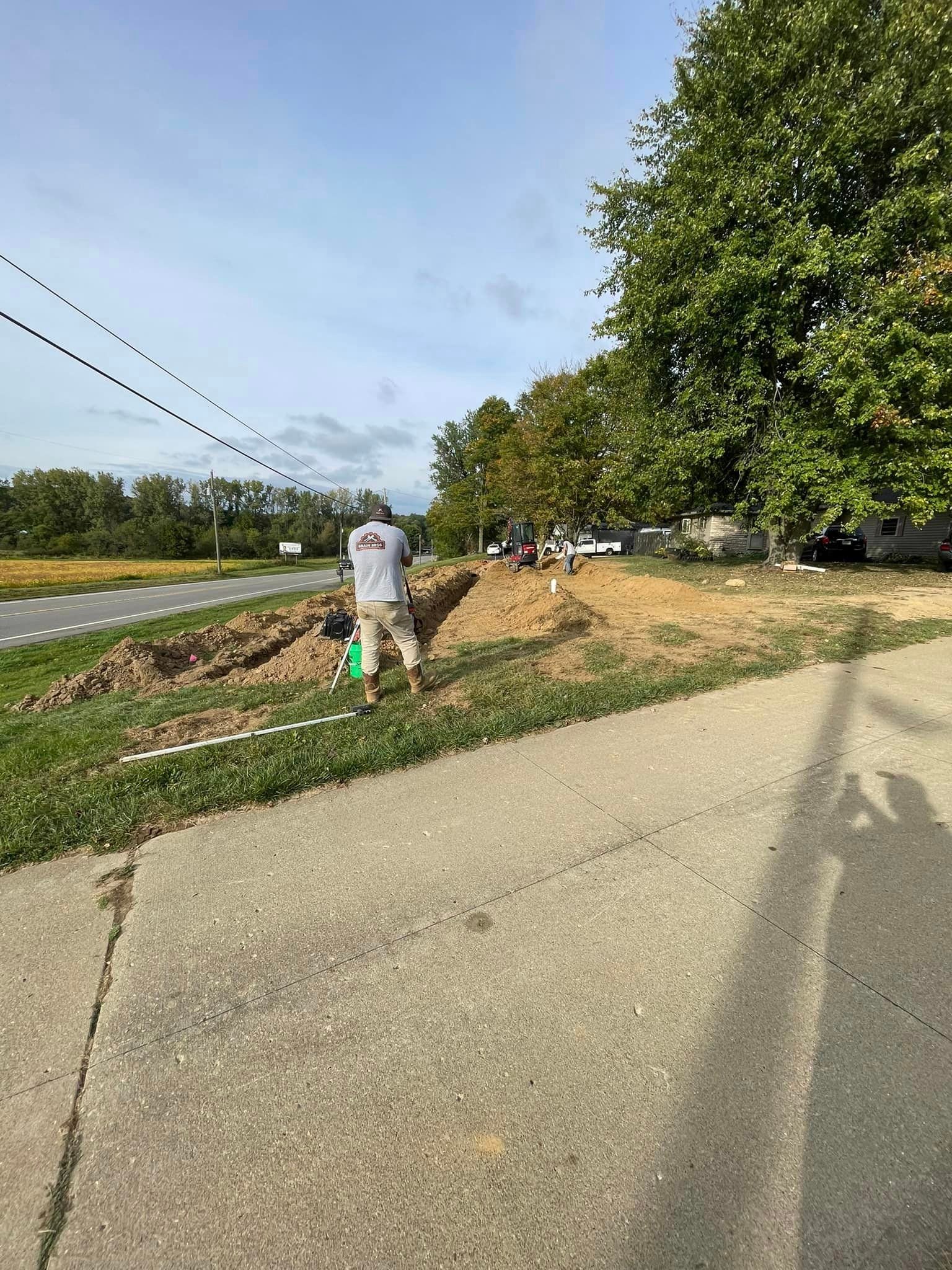 Drain Bros llc workers are installing or repairing a septic system on a grassy hill with equipment and tools in use.