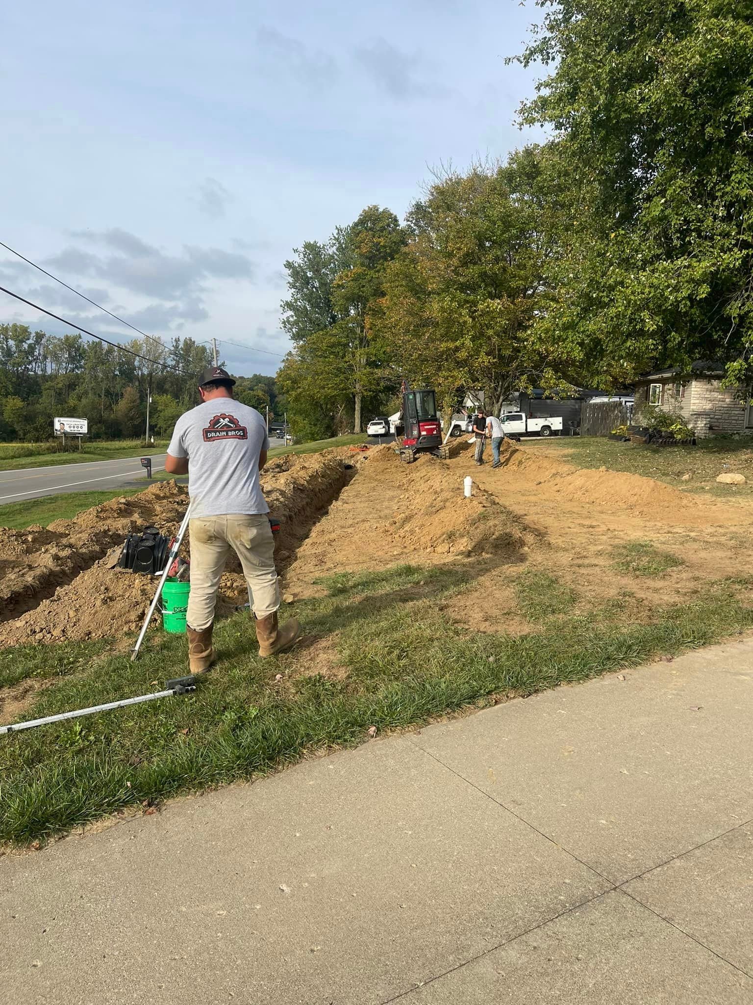 Drain Bros llc workers help with home excavation near the road, showing teamwork and professional service.