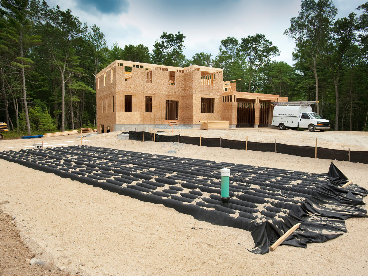 Drain Bros llc installing a drainage system at a new house build, using pipes and black sheeting on the sandy ground.