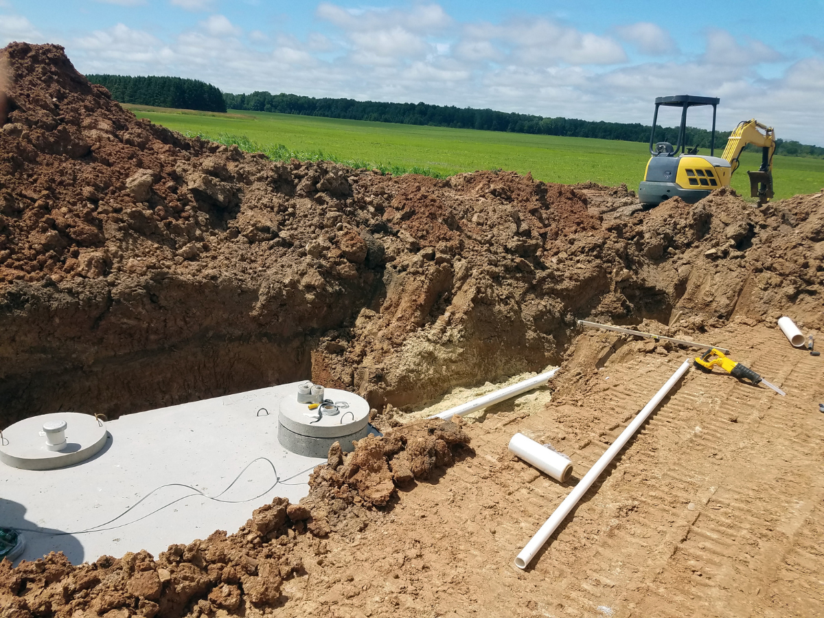 Drain Bros llc installs a new septic system in the country, with equipment and plumbing work visible near open land.