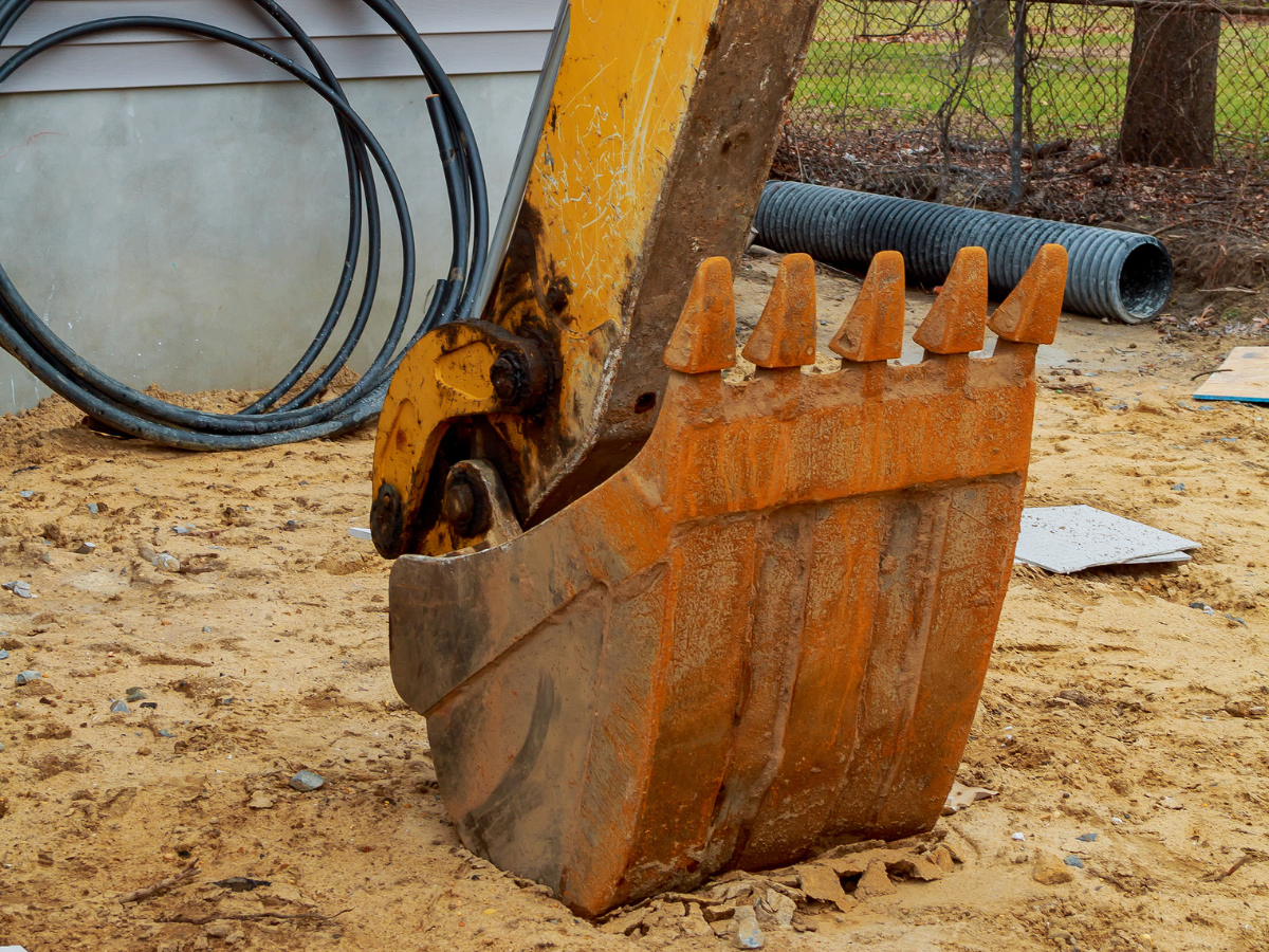 Drain Bros llc digging for a new drainage system at a sandy construction site with pipes ready to be installed.